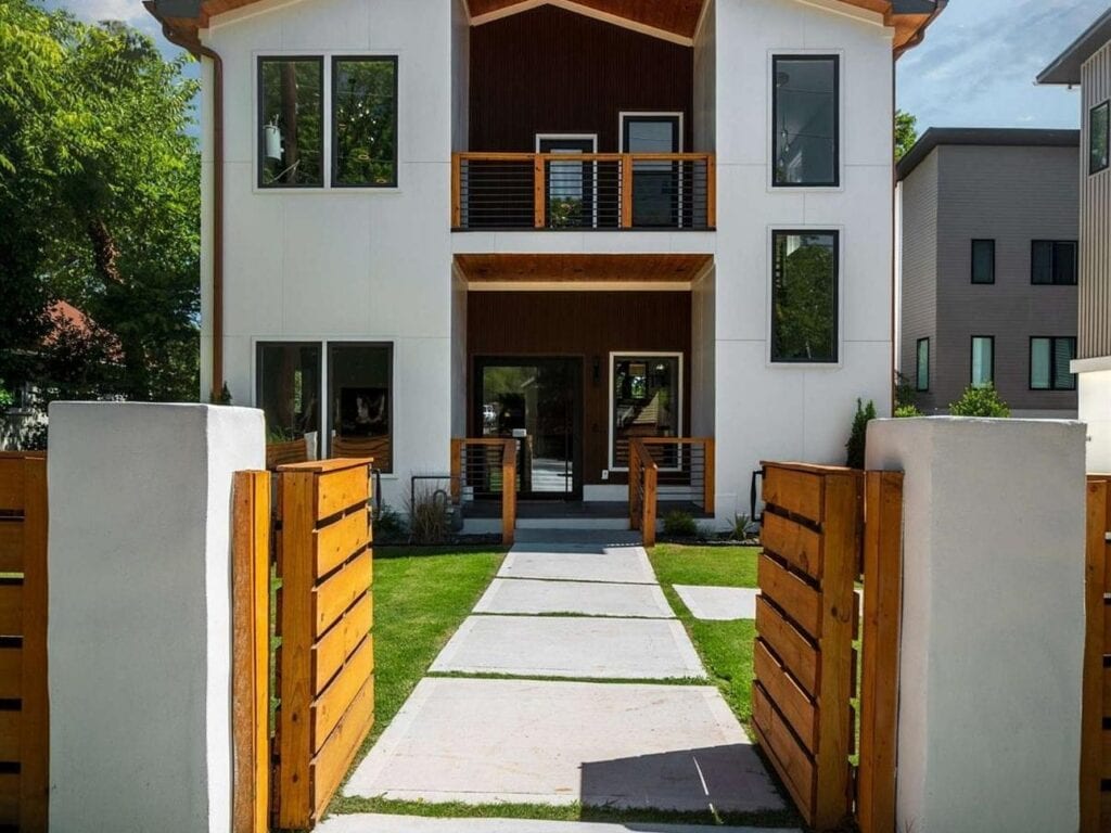 Memorial Drive Residence entry walk between white masonry piers and wood gates toward the two-story gabled facade.